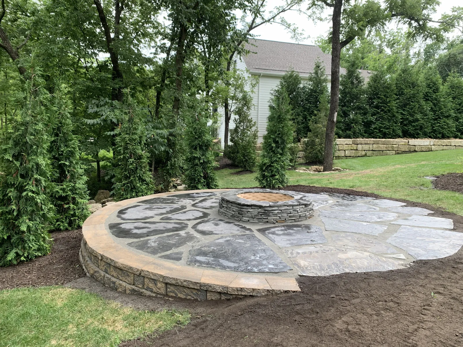 Backyard flagstone patio with fire pit and privacy landscaping completed in Merriam by Volz Lawn & Landscape