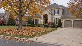 Leawood, KS stone-front home with a thick layer of fallen maple leaves covering the yard and driveway