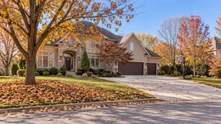Olathe, KS two-story home surrounded by fall color with leaves scattered across the lawn and drive